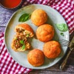 Frittierte Arancini mit Hackfleisch-Füllung und Mozzarella, garniert mit Basilikum und Dip.