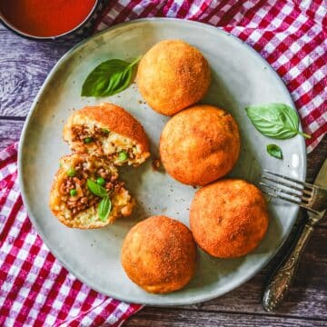 Frittierte Arancini mit Hackfleisch-Füllung und Mozzarella, garniert mit Basilikum und Dip.