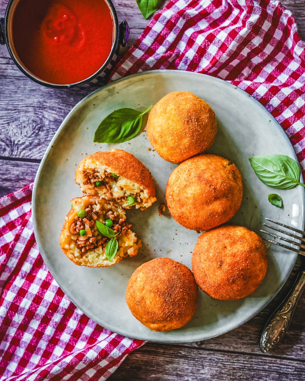 Knusprig frittierte Arancini mit Hackfleisch-Füllung, garniert mit Basilikum, serviert mit Tomatensoße.