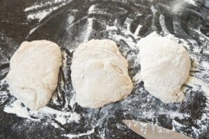 Drei Baguette-Teigstücke auf bemehlter Arbeitsfläche vor dem Formen und Backen nach Baguette Rezept.
