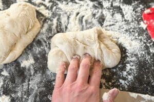 Hand drückt Baguette-Teig auf bemehlter Arbeitsfläche während der Zubereitung nach Baguette Rezept.