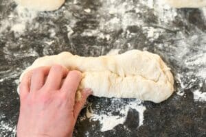 Hand knetet hellen Baguette-Teig auf bemehlter dunkler Arbeitsfläche während der Zubereitung.