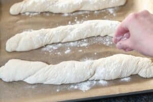Handgeformte Baguettes auf bemehlter Arbeitsfläche vor dem Backen nach einem einfachen Baguette Rezept.