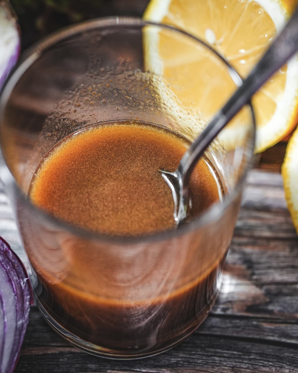 Balsamico-Dressing in einem Glas mit Strohhalm, garniert mit Zitronenscheiben auf Holzuntergrund.