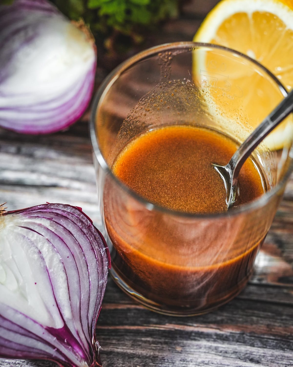 Balsamico-Dressing in Glas mit Zitrone und roten Zwiebeln auf Holzuntergrund.