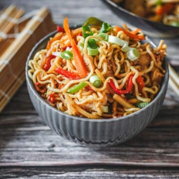 Gebratene Bami Goreng mit Hähnchen, Paprika und Frühlingszwiebeln in einer Schüssel mit Stäbchen.