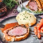 Filet Wellington mit rosa Fleischkern, Kartoffelpüree und Karotten auf schwarzem Teller serviert.