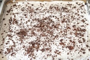 Cremiger Fingerleckenkuchen mit einer Schicht aus Sahne und gehackter Schokolade auf einem Blech.