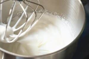 Steifgeschlagene Sahne mit Mixer in Schüssel für Fingerleckenkuchen-Creme
