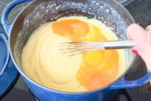 Fingerlickenkuchen-Teig wird in blauem Topf mit Schneebesen verrührt, cremige Masse mit Eiern gemischt.