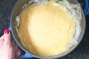 Cremige Fingerleckenkuchen-Masse in blauer Schüssel mit Frischhaltefolie abgedeckt
