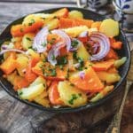 Herbstlicher Kürbis-Kartoffel-Salat mit roten Zwiebeln und Schnittlauch in blauer Schale auf Holzbrett serviert.