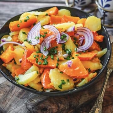 Herbstlicher Kürbis-Kartoffel-Salat mit roten Zwiebeln und Schnittlauch in blauer Schale auf Holzbrett serviert.