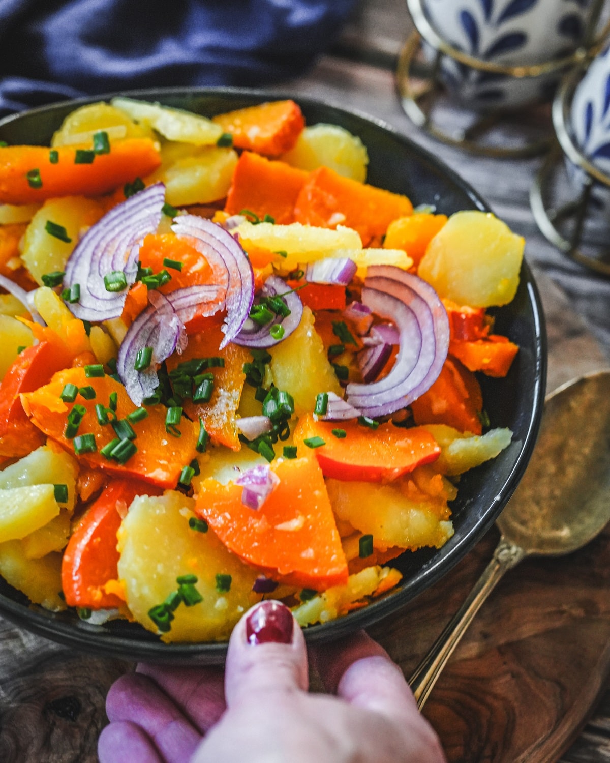 Kürbis-Kartoffel-Salat mit roten Zwiebeln und Schnittlauch auf blauem Teller serviert.