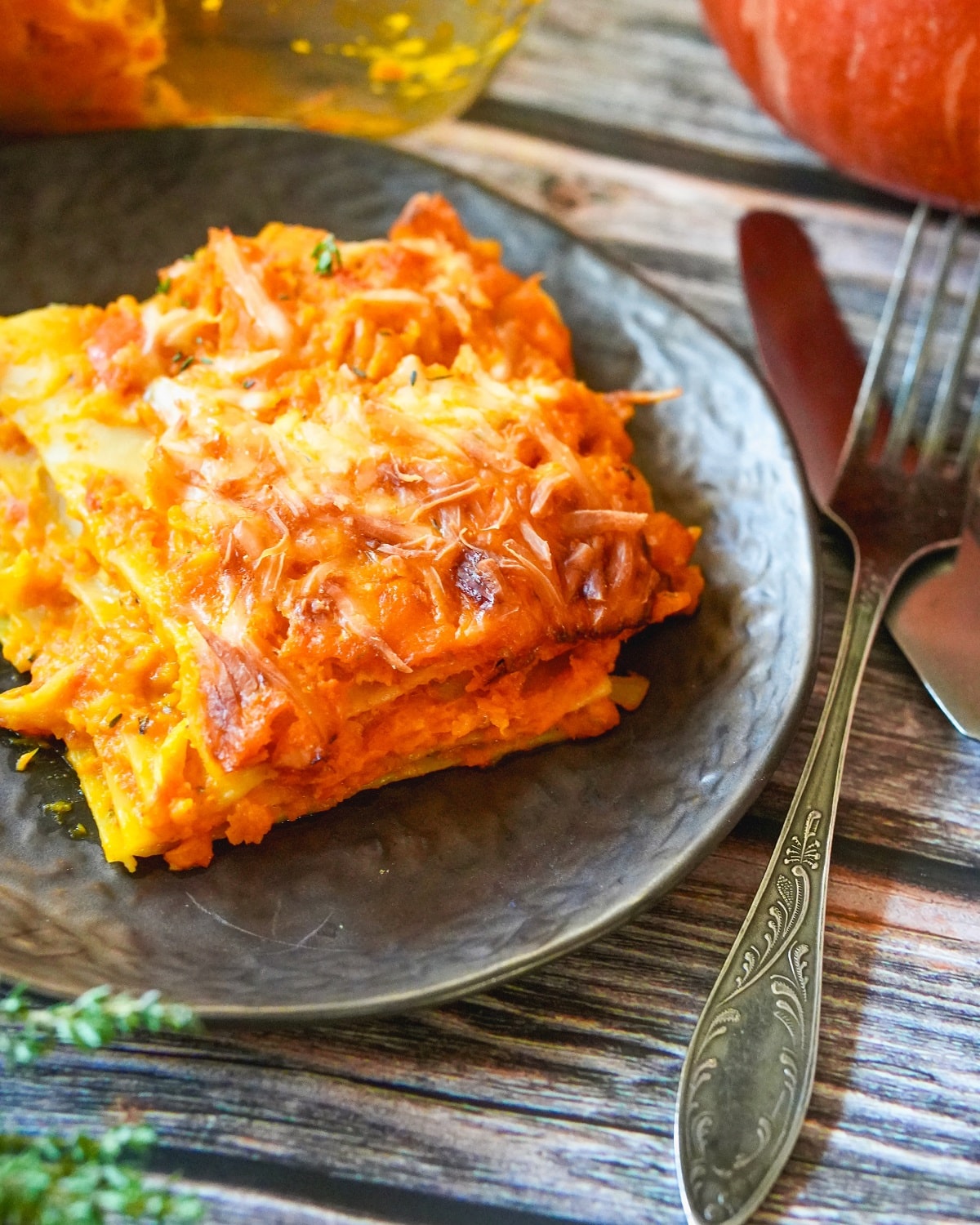 Herbstliche K&uuml;rbis-Lasagne mit goldbrauner K&auml;sekruste auf grauem Teller serviert.