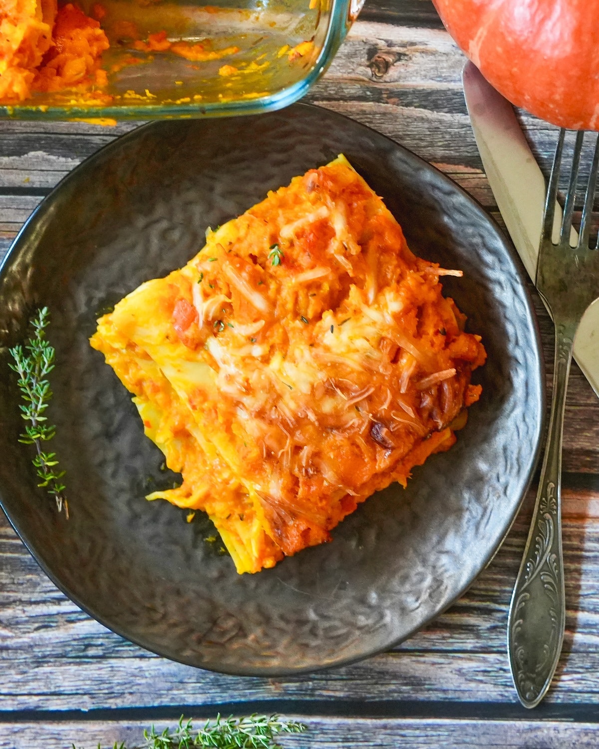 Goldbraun gebackene K&uuml;rbis-Lasagne mit Hokkaido-K&uuml;rbis auf schwarzem Teller, garniert mit Thymian.
