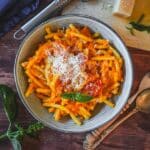 Cremige Kürbis-Pasta mit Parmesanspänen, frischem Basilikum in weißer Schale serviert.