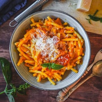 Cremige Kürbis-Pasta mit Parmesanspänen, frischem Basilikum in weißer Schale serviert.