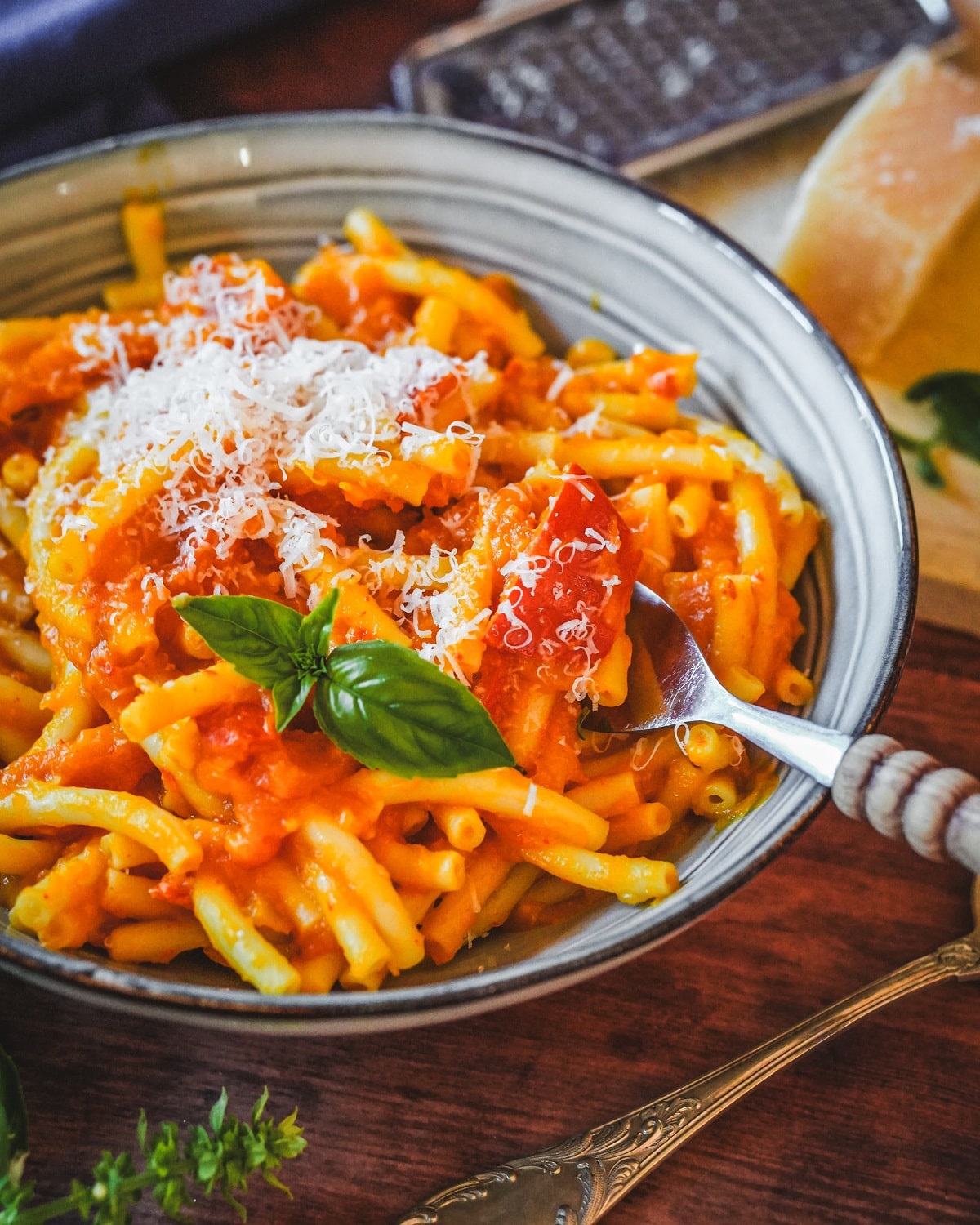 Cremige Kürbis-Pasta mit Parmesanspänen, frischem Basilikum in weißer Schale serviert.