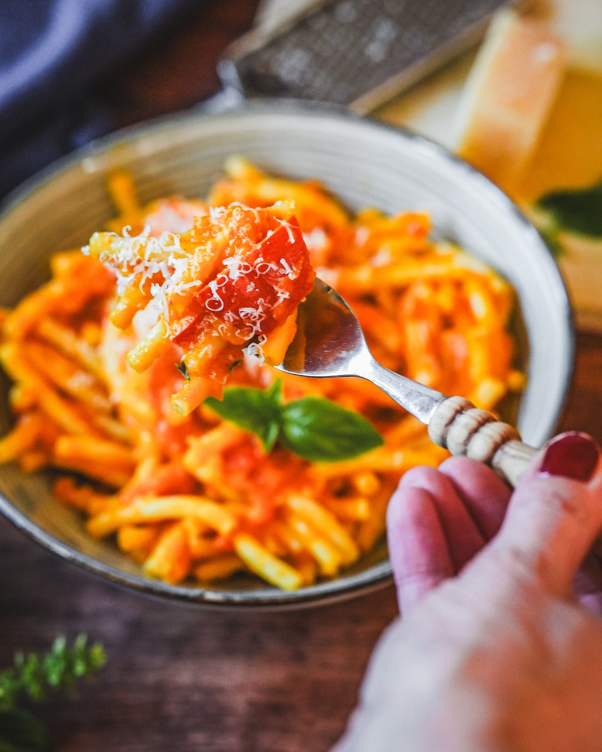 Cremige Kürbis-Pasta mit Parmesan und frischen Kräutern auf Gabel über Schüssel serviert.