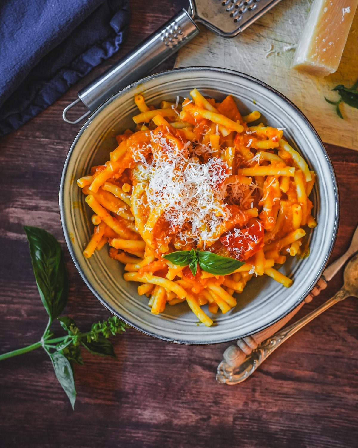 Cremige Kürbis-Pasta mit Parmesanraspel und frischem Basilikum auf Holzuntergrund serviert.