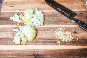 Den Backofen auf 180 °C Ober-/Unterhitze vorheizen, Zwiebel und Knoblauch schälen und fein hacken.