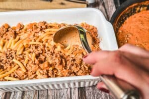 Makkaroni Auflauf mit Hackfleisch wird in einer Auflaufform serviert, während eine Portion mit einem Löffel entnommen wird.