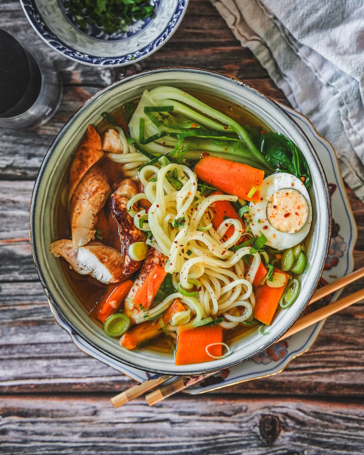 Ramen Suppe mit Hähnchen, Nudeln, Gemüse und Brühe in einer asiatischen Schale mit Stäbchen serviert.