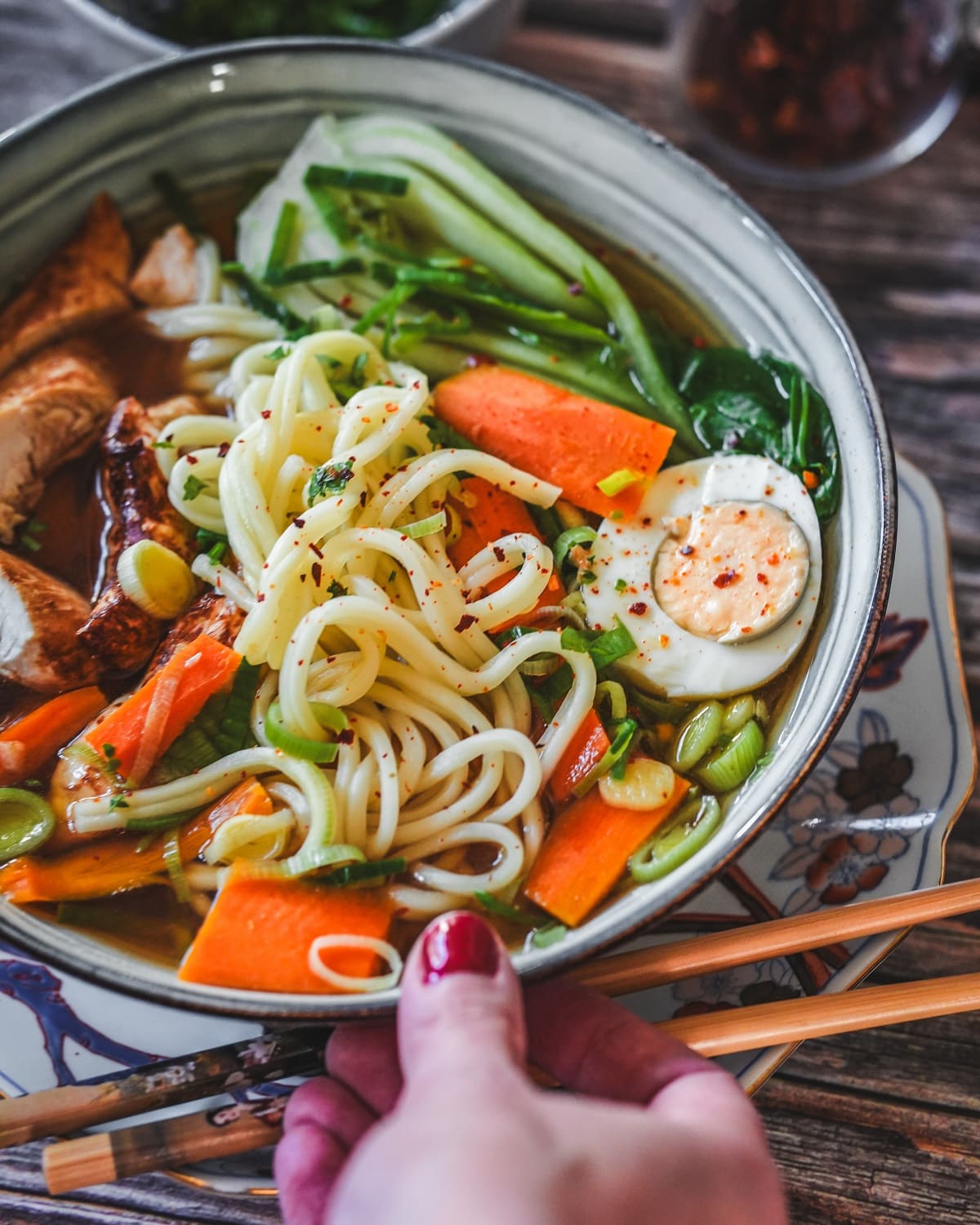 Schüssel mit Ramen Suppe mit Hähnchen, Ei, Gemüse und Nudeln in aromatischer Brühe mit Stäbchen.