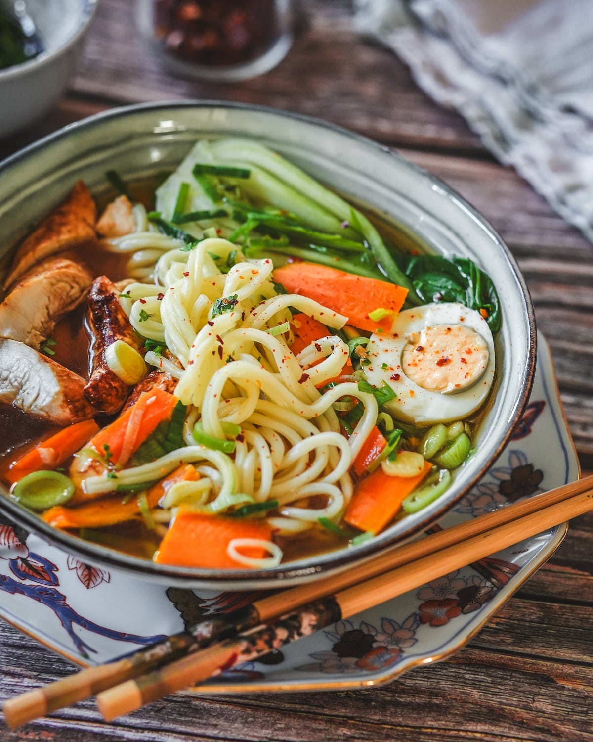 Asiatische Ramen Suppe mit Hähnchen, Nudeln, Gemüse und Brühe in einer Schüssel mit Stäbchen.