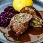 Rinderrouladen mit Soße, Rotkohl und Knödel auf Teller angerichtet.