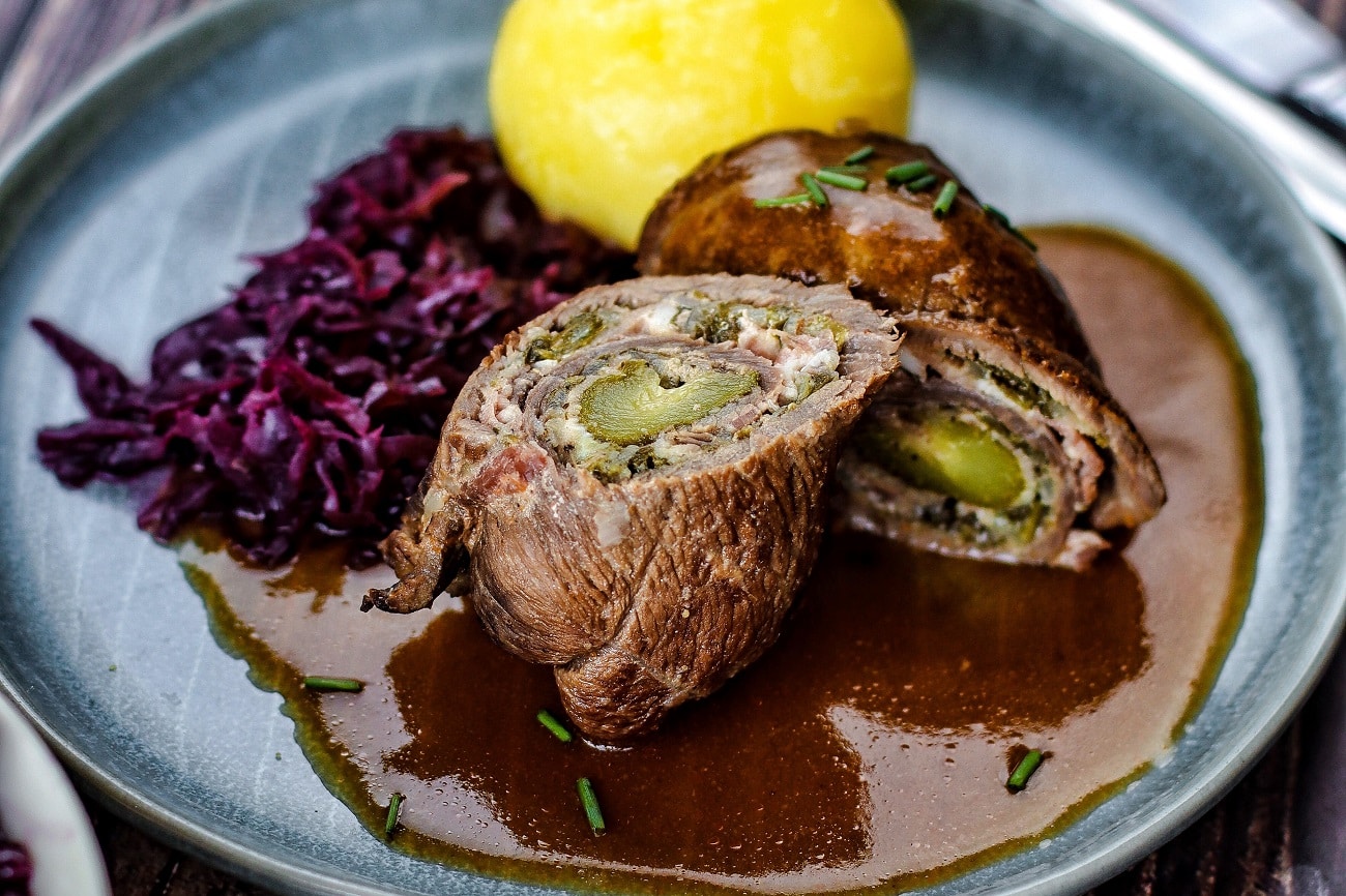 Rinderrouladen mit Soße, Rotkohl und Knödel auf Teller angerichtet.