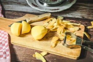 Kartoffeln werden auf Holzbrett geschält und in Stücke geschnitten zur Zubereitung von Salzkartoffeln.