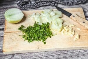 Vorbereitete Zutaten für Spanakopita auf Schneidebrett: gehackte Petersilie, geschnittene Zwiebel, Knoblauch und halbe Zwiebel.