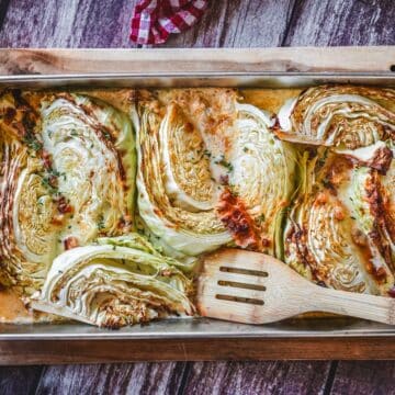 Gerösteter Spitzkohl mit Speck und Parmesan auf Backblech mit Holzspatel.
