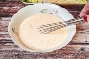 Die angerührte Speisestärke zurück zur Sahne-Brühe-Mischung geben. Gepressten Knoblauch, Senf, Paprikapulver, Salz, Pfeffer und Muskatnuss hinzufügen und gründlich verrühren. Zum Schluss den frisch geriebenen Parmesan untermischen.