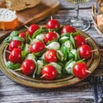 Tomate-Mozzarella-Spieße mit Basilikum auf Teller, serviert mit Brot und Wein.