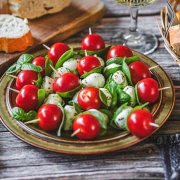 Tomate-Mozzarella-Spieße mit Basilikum auf Teller, serviert mit Brot und Wein.
