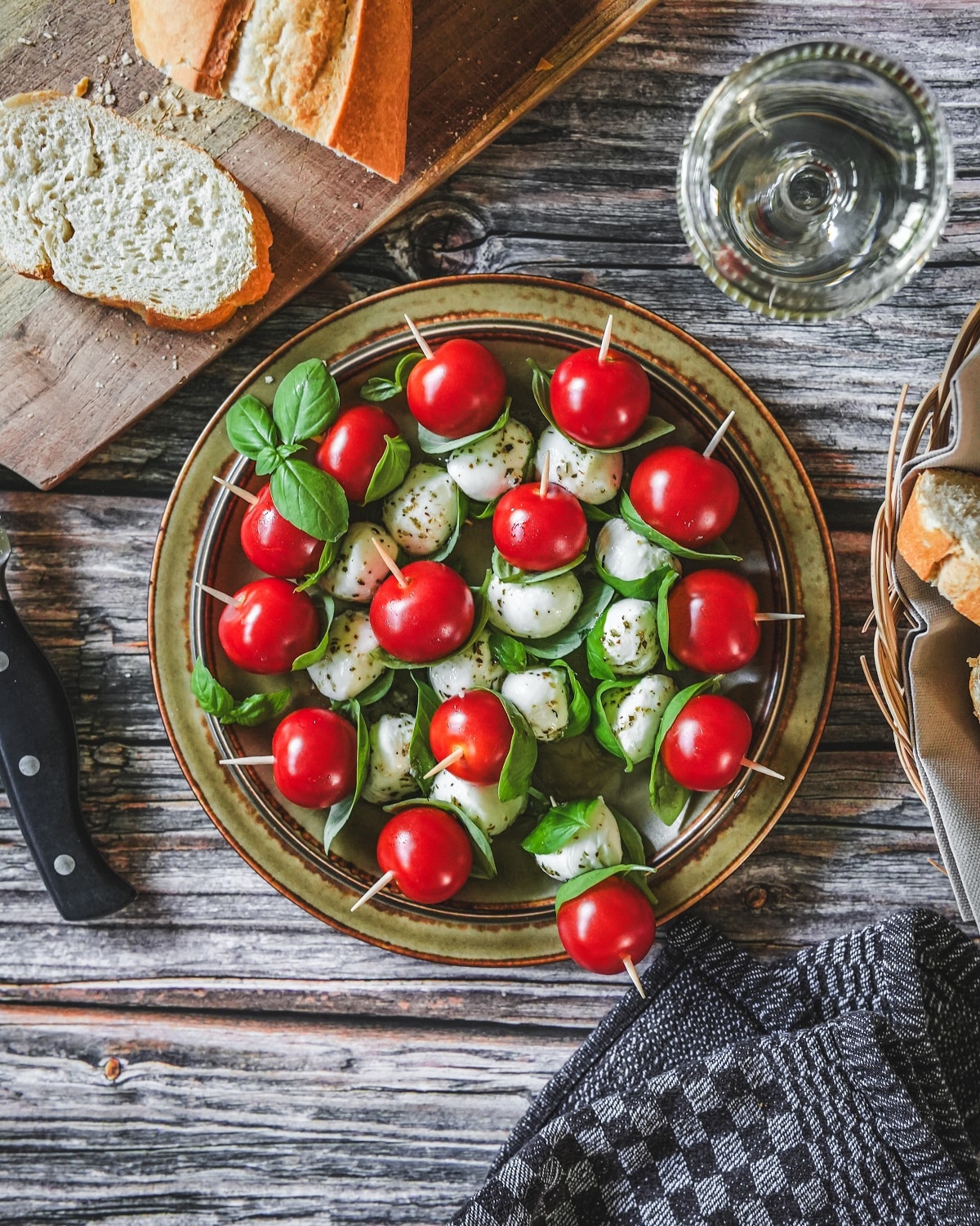 Tomate-Mozzarella-Spieße mit Basilikum auf Teller, serviert mit Brot und Wein.