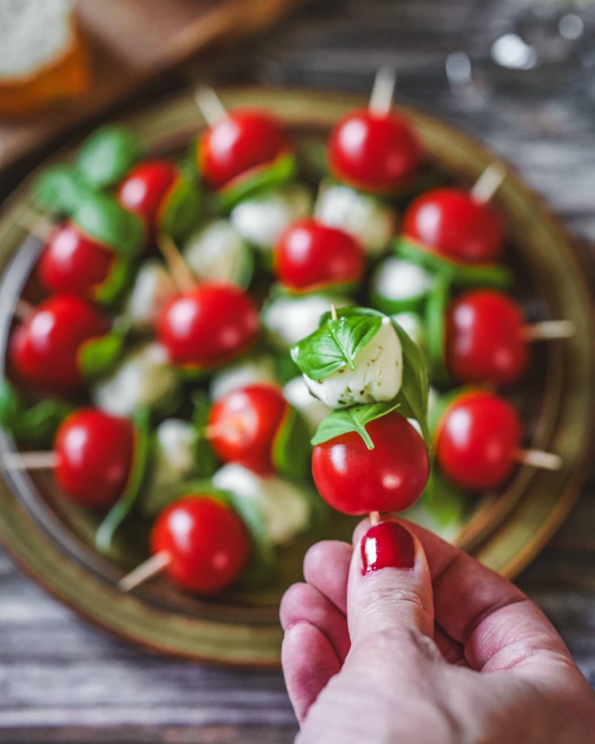 Tomaten-Mozzarella-Spieße mit Basilikum auf Holzspießen, eine Hand hält einen Spieß.