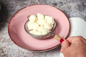 Mozzarella-Kugeln werden in einem Sieb über einer Schüssel abgetropft.