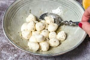 Die Mozzarellakugeln mit der Marinade vermengen und etwa 15 bis 30 Minuten ziehen lassen.