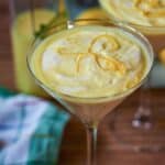 Cremiges Zitronendessert im Glas mit Zitronenzesten garniert, serviert auf Holzuntergrund mit Orangenfrüchten.