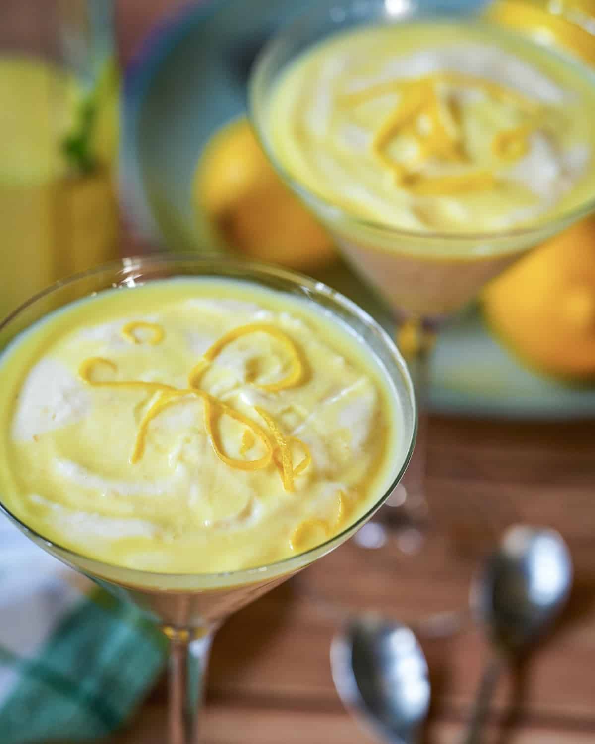 Zitronencreme-Dessert im Glas mit Zitronenscheiben und Schlagsahne, serviert mit frischen Zitronen.