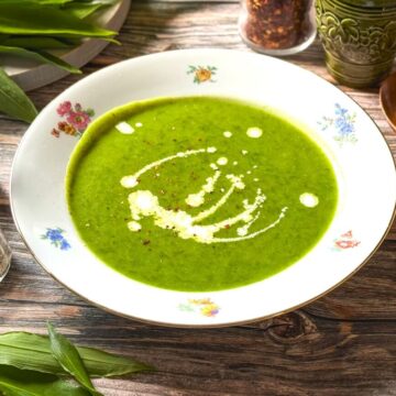 Grüne Brennnessel-Kartoffelsuppe mit Schmand-Garnitur auf Vintage-Porzellan serviert.