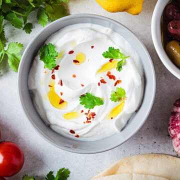 Hummus-Dip mit Olivenöl, Granatapfelkernen und Koriander, umgeben von Tomaten, Oliven und Fladenbrot.