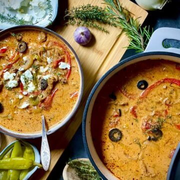 Zwei Töpfe mit mediterrane Gemüsesuppe, garniert mit Feta, Oliven und frischen Kräutern auf Holztisch.