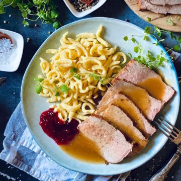 aufgeschnittener Kalbsbraten liegt auf Teller neben Spätzle.