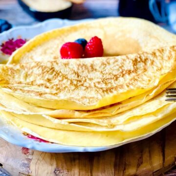 Klassische französische Crêpes mit Puderzucker und frischen Beeren auf rustikalem Holzteller serviert.