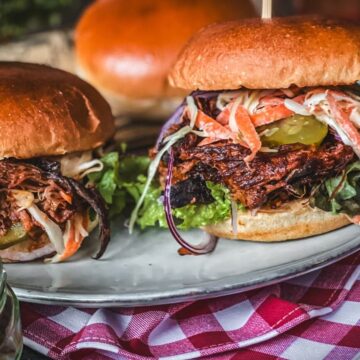 Zwei saftige Pulled Pork Burger mit Coleslaw, Gurken und Zwiebeln auf Brioche-Brötchen serviert.